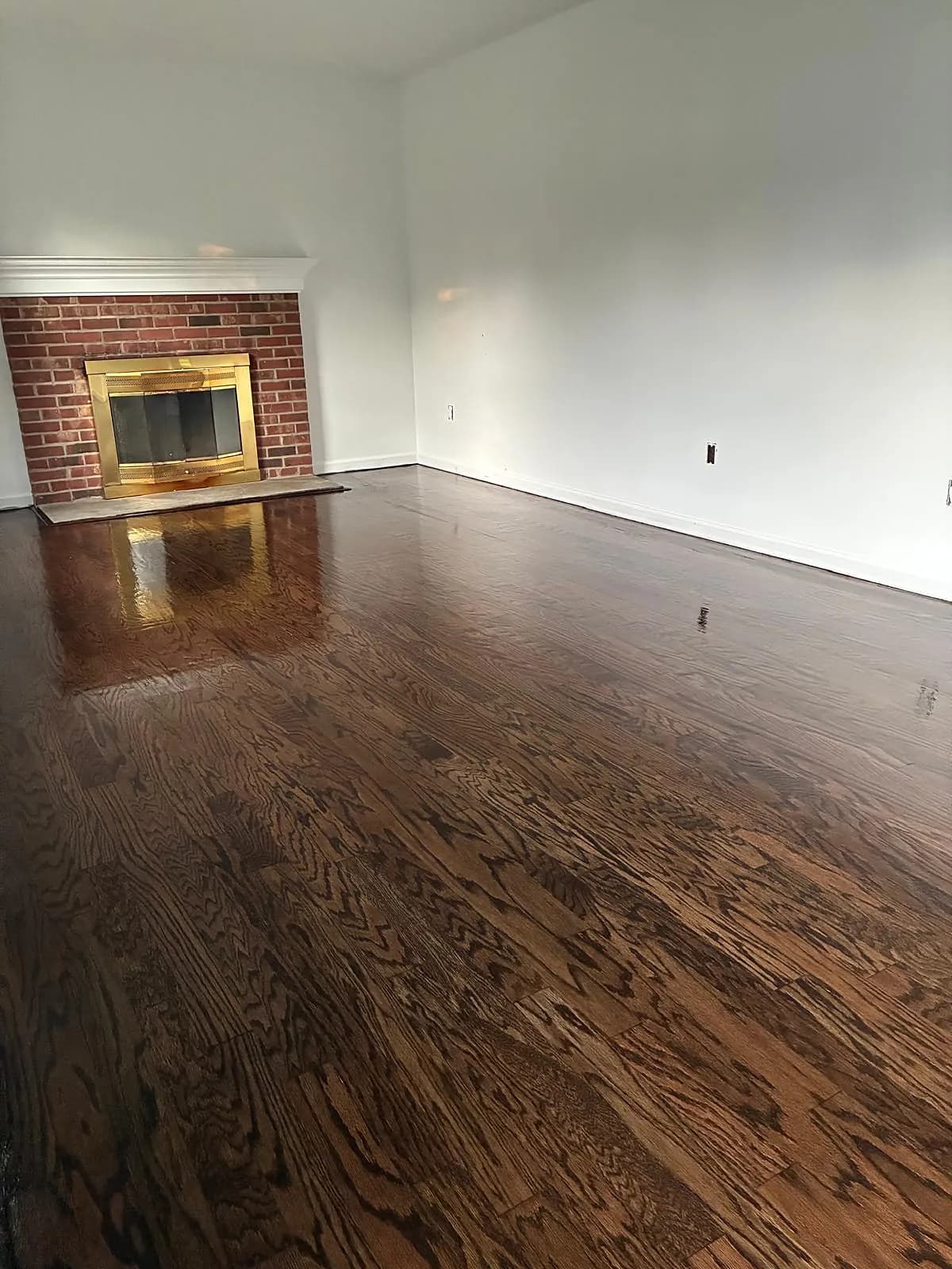 Oak living room floor refinished to a rich dark walnut stain next to a brick fireplace